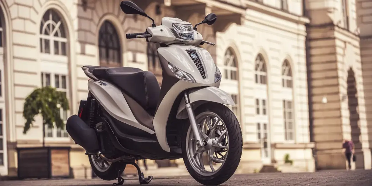 Biały skuter Piaggio Medley zaparkowany na bruku przed zabytkową kamienicą.