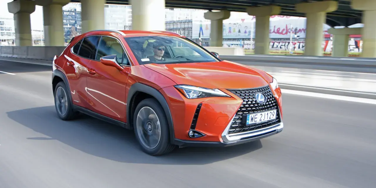 Pomarańczowy Lexus UX 250h jedzie po miejskiej drodze pod wiaduktem.