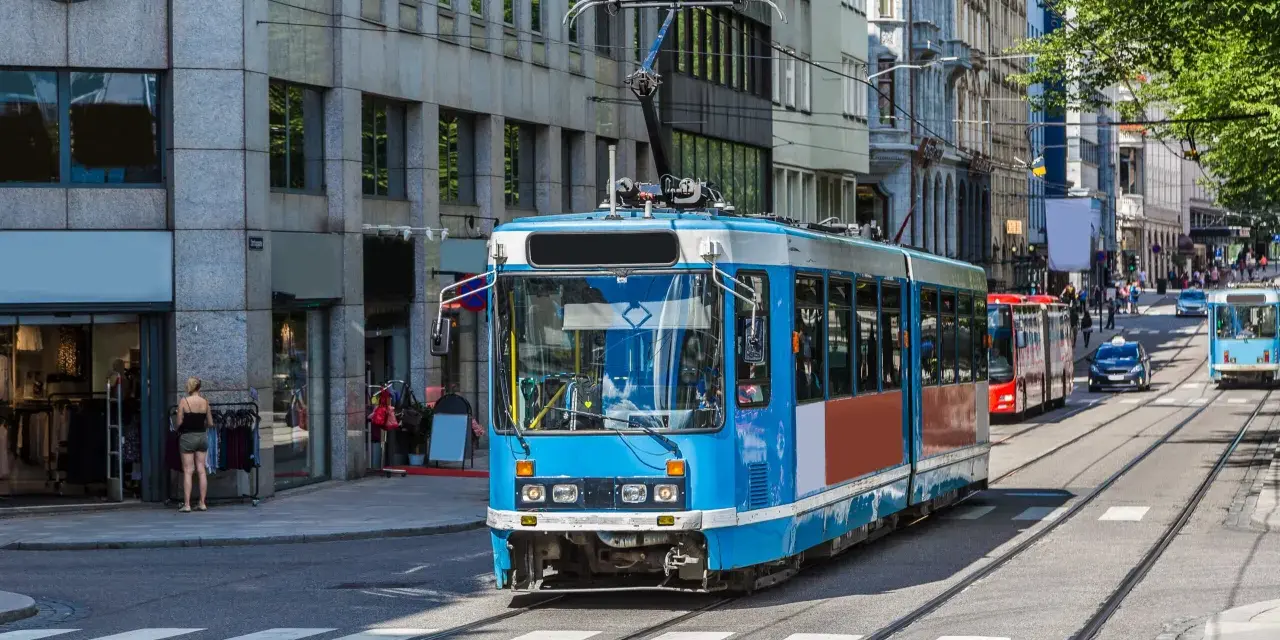 Błękitny tramwaj na tle budynków w Oslo. To część sprawnie działającej oslo komunikacji miejskiej, która przewozi mieszkańców i turystów.