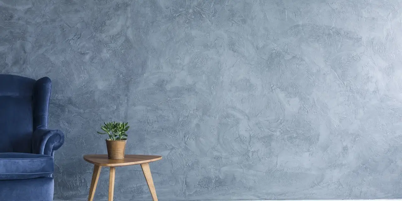Fauteuil bleu profond devant un mur texturé avec une peinture effet stucco. Une petite table en bois supporte une plante verte.