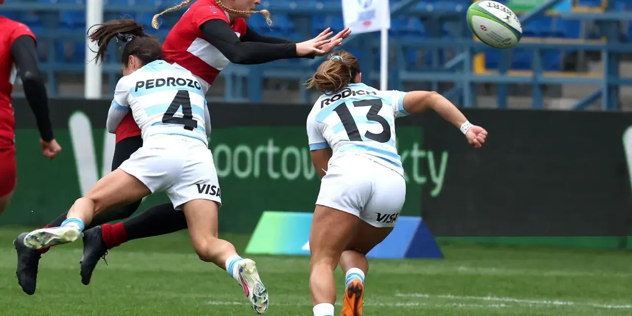 Zacięta walka o piłkę podczas rugby mistrzostwa świata. Zawodniczka w czerwonej koszulce próbuje przechwycić piłkę, podczas gdy dwie rywalki w białych strojach próbują ją zatrzymać.