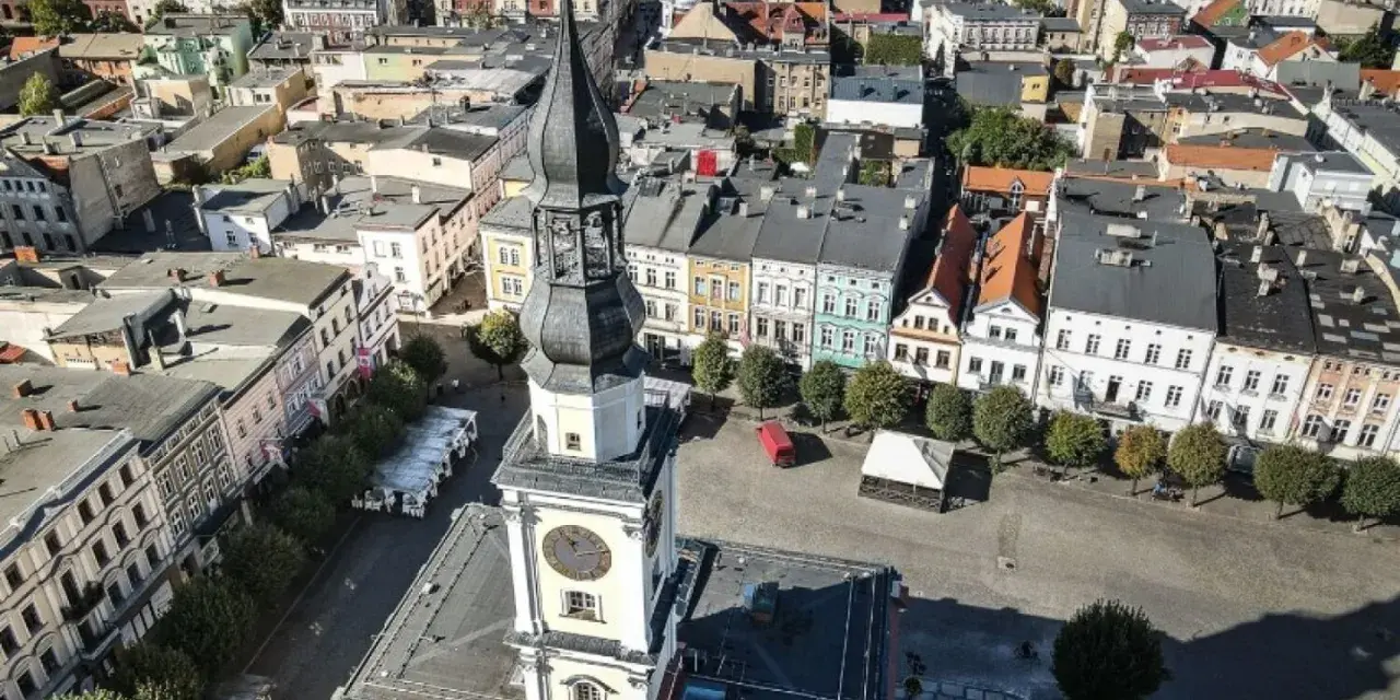 Widok z lotu ptaka na rynek w Lesznie. Wieża ratusza góruje nad kolorowymi kamienicami, ukazując urokliwe leszno atrakcje.