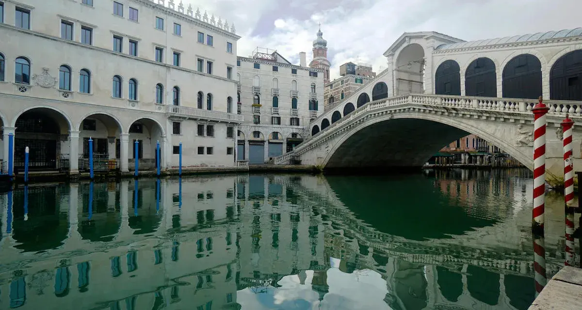 Le vie di Venezia, con il Ponte di Rialto che si specchia sull'acqua verde e gli edifici storici che creano un'atmosfera magica.