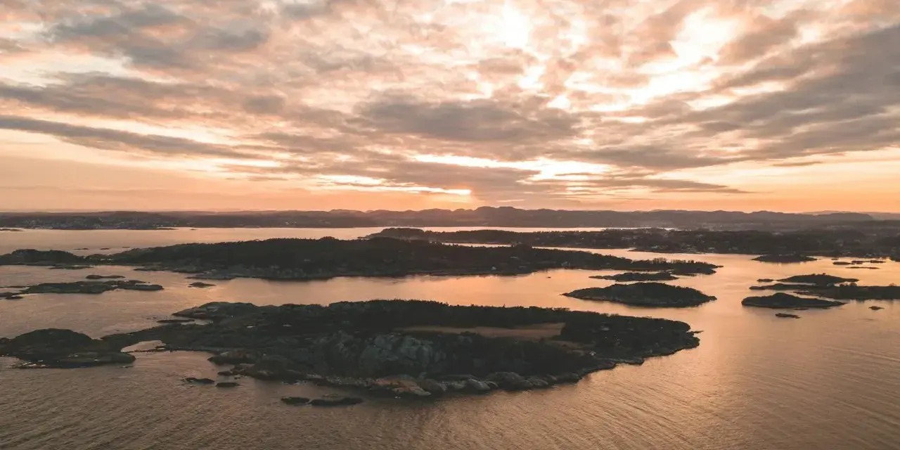 Zachód słońca nad archipelagiem, przypominającym szwedzkie fiordy. Woda odbija złote światło, a chmury malują niebo.