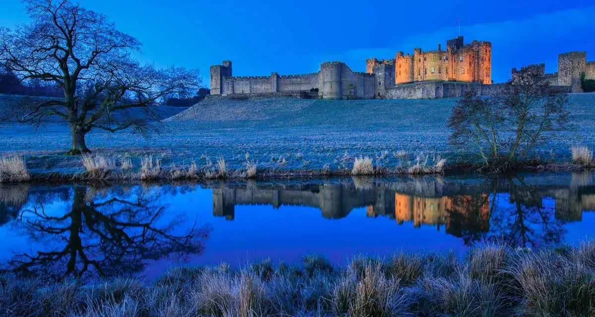 Un château majestueux se reflète dans l'eau calme, sous un ciel d'un bleu profond. Une scène paisible de **heure bleue photo**.