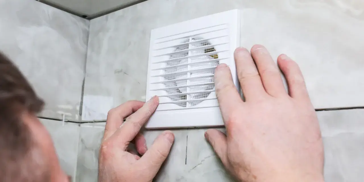 Installation d'un nouveau ventilateur pour la **salle de bain ventilation**. Mains ajustant l'appareil blanc sur un mur carrelé.
