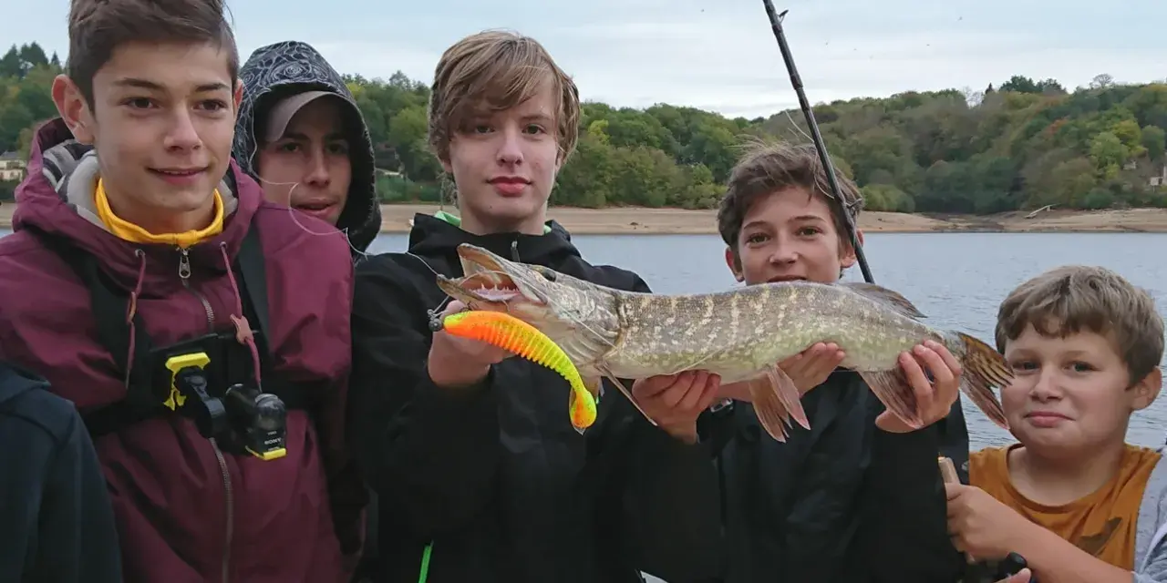 Des jeunes pêcheurs fiers de leur prise lors d'une colonie de vacances pêche. Un beau brochet exhibé devant un lac.
