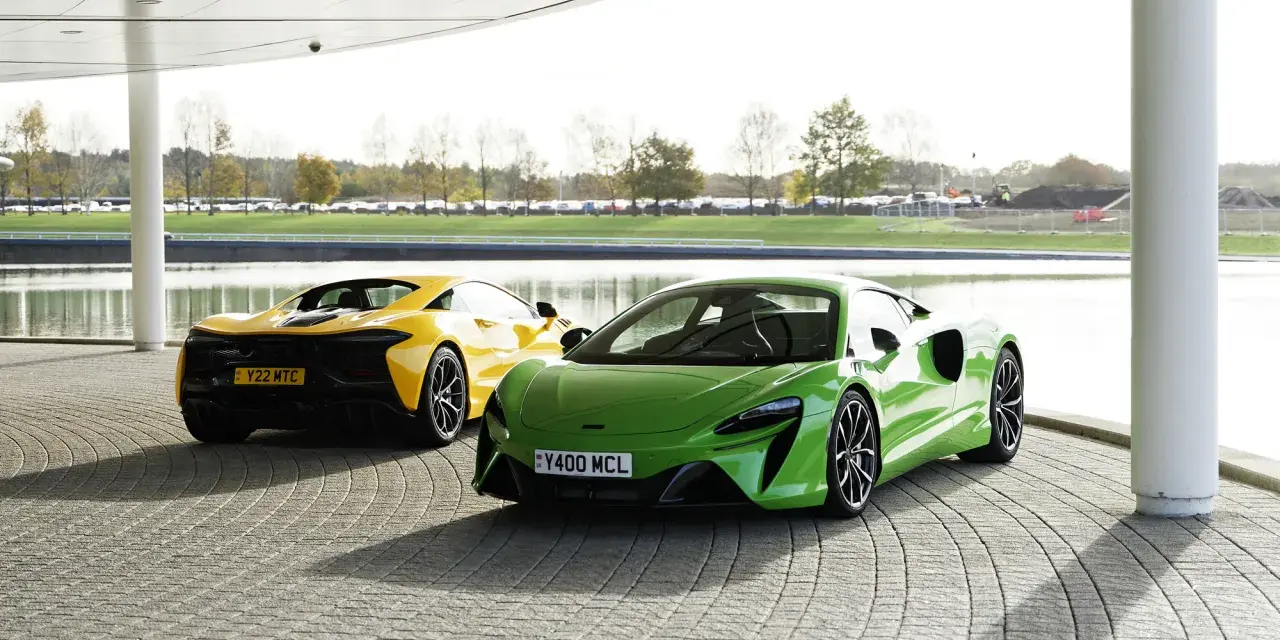 Dwa sportowe samochody McLaren Artura: jeden zielony z przodu, drugi żółty z tyłu, stojące na zewnątrz.