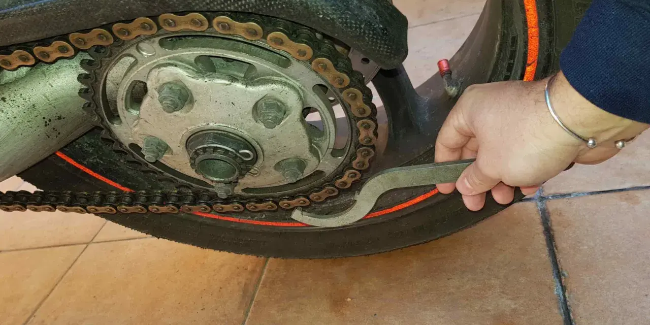 Mano con chiave speciale per regolare la catena della moto, mostrando come tirare la catena.