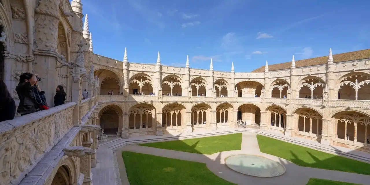 The Jerónimos Monastery, a stunning monastery in Portugal, features a grand courtyard with intricate stonework and a lush green lawn.