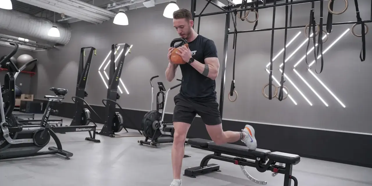 Man tränar utfall med kettlebell i ett modernt gym. Han fokuserar på att bygga en stor rumpa.