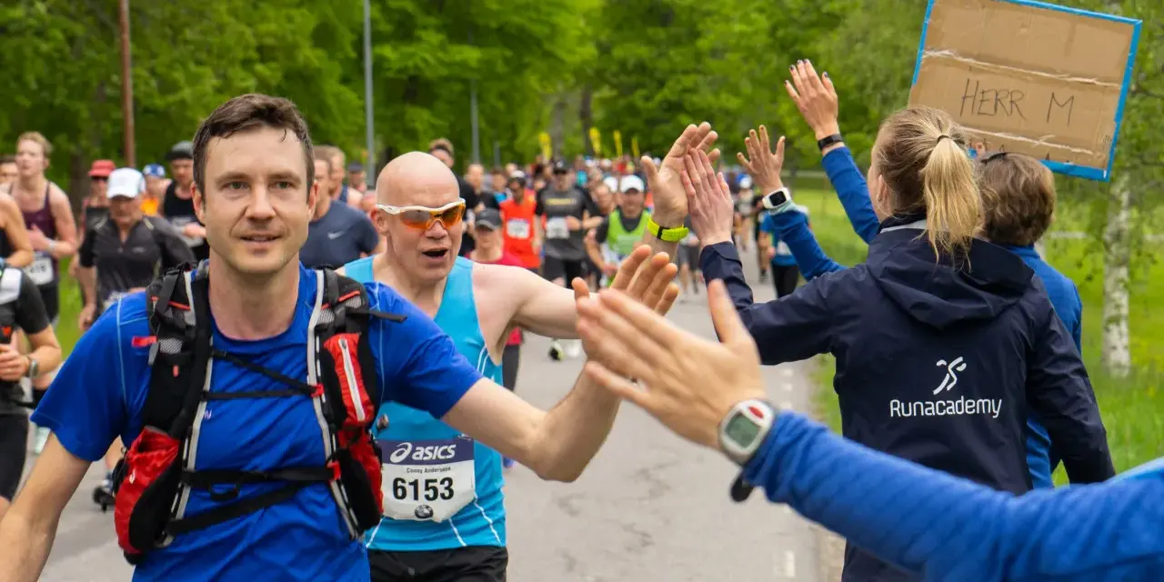 Glada löpare ger high-fives under loppet. Sista veckan innan halvmarathon, peppas deltagarna av publiken.