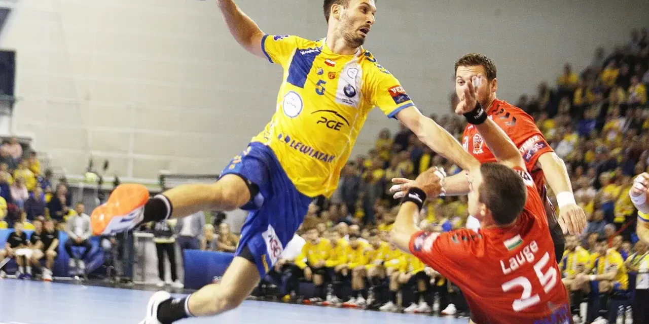 Piłkarz ręczny Telekom Veszprem w żółtej koszulce skacze do rzutu, broniony przez zawodnika w czerwonej.