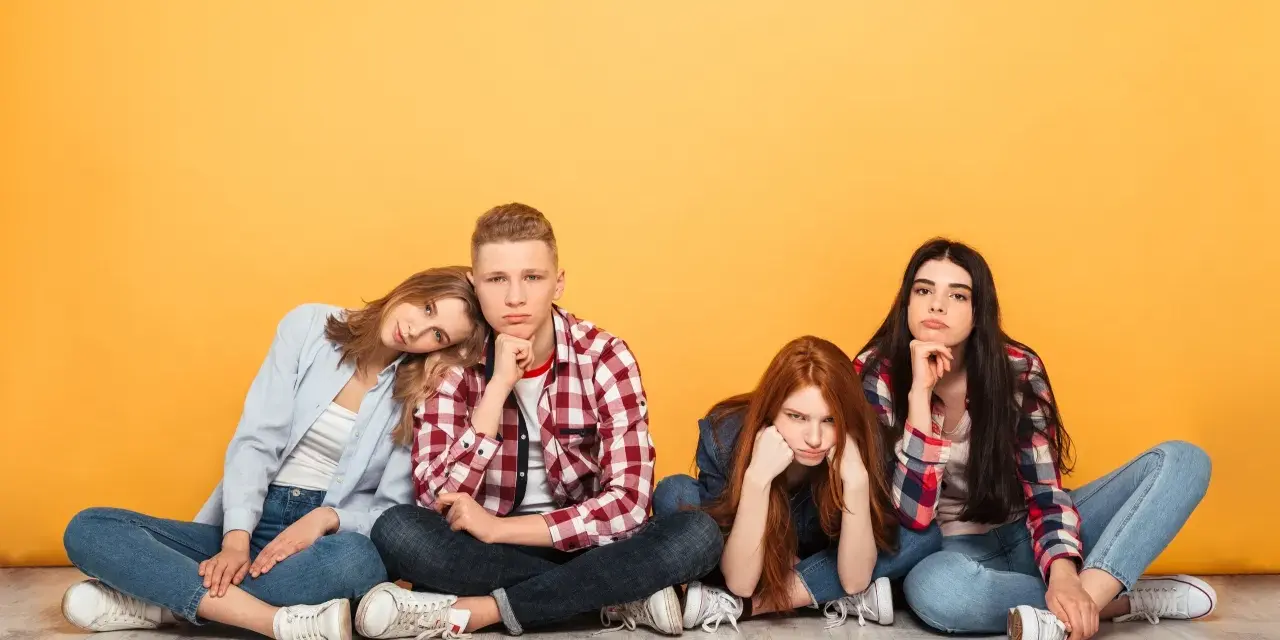 Vier junge Leute sitzen auf dem Boden, die Gesichter zeigen deutliche Langeweile.