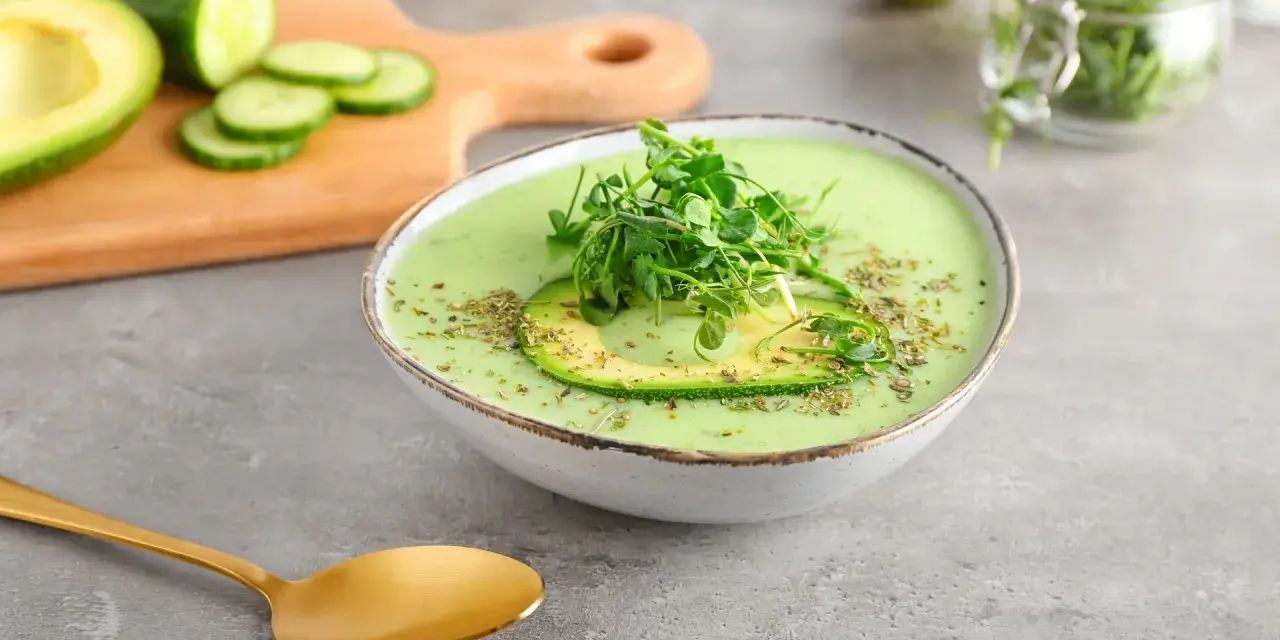 Gazpacho de aguacate cremoso con rodaja de aguacate y brotes verdes, servido en un cuenco blanco.