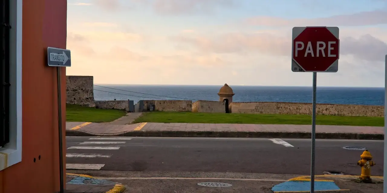 A "PARE" sign stands by the ocean in Puerto Rico. Should I rent a car to explore this beautiful island?