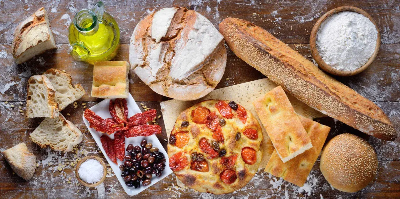 Apulia jedzenie: świeże pieczywo, focaccia z pomidorami, oliwki, suszone pomidory i oliwa z oliwek na drewnianym stole.