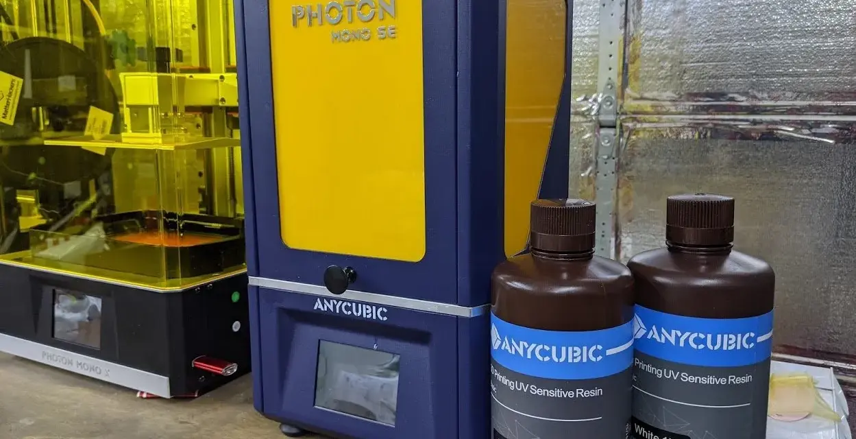 Dwa drukarki 3D Anycubic, w tym Anycubic Photon Mono SE, oraz butelki z żywicą do druku.
