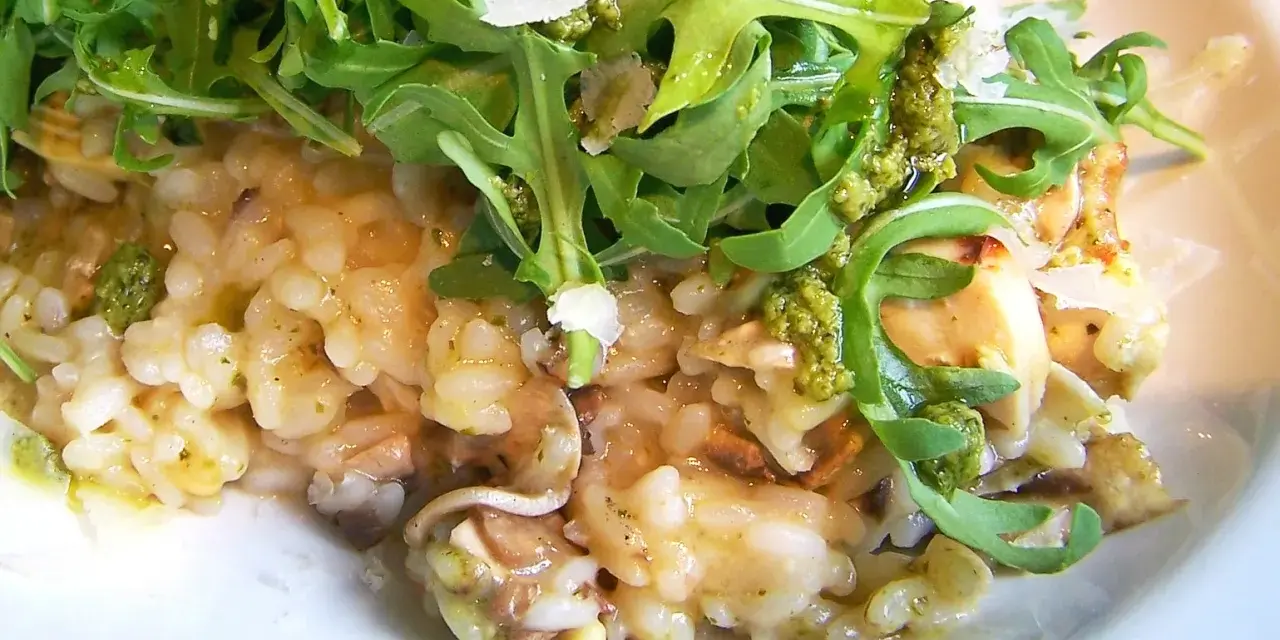 Kremowe risotto z kurczakiem i pieczarkami, udekorowane rukolą i parmezanem.