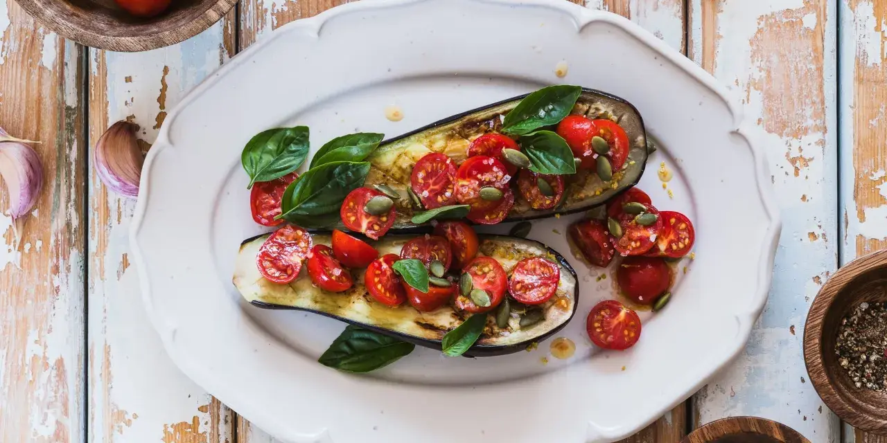Melanzane ripiene vegetariane con pomodorini, basilico e semi di zucca, un piatto colorato e saporito.