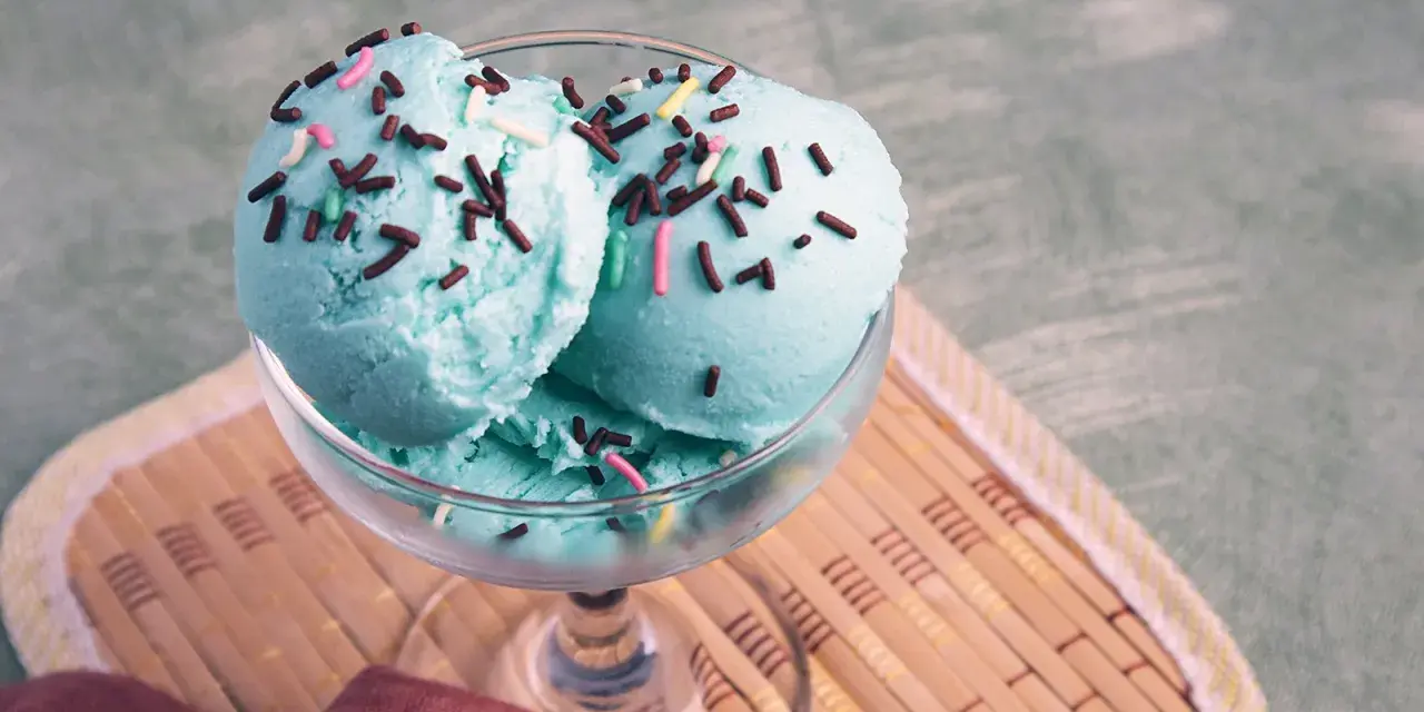 Ein Glas mit drei Kugeln blaues Eis, bestreut mit Schokostreuseln und bunten Zuckerstreuseln.
