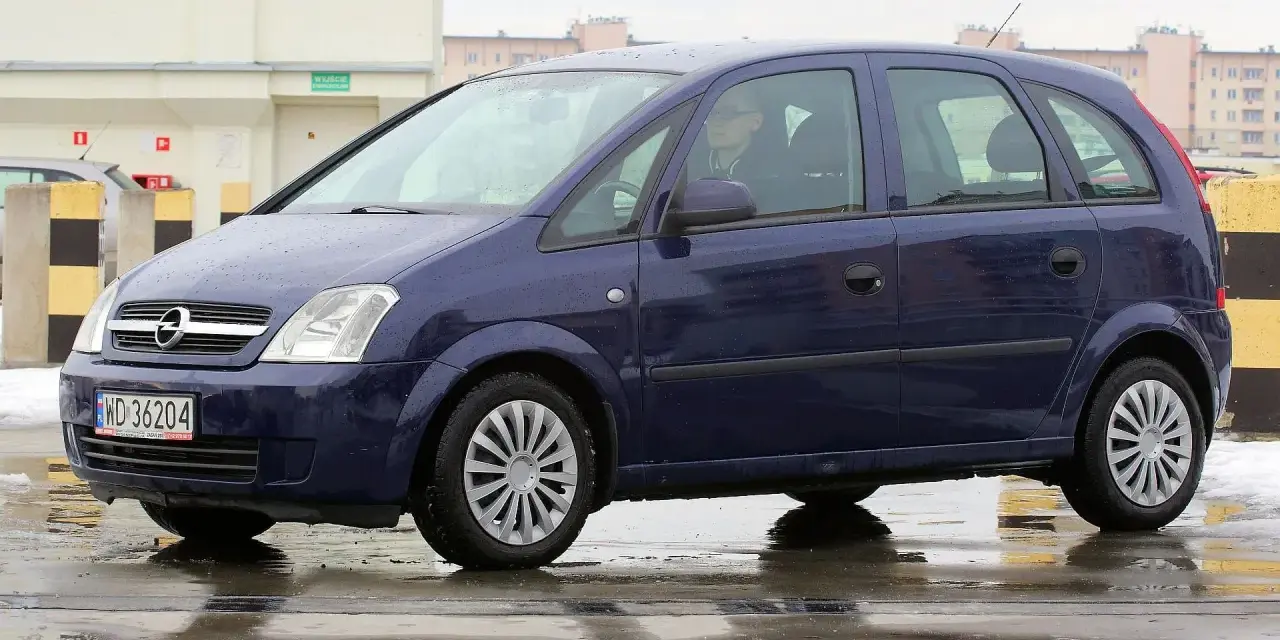 Granatowy Opel Meriva na mokrej nawierzchni. Kierowca w okularach. Wiele pozytywnych opinii o tym modelu.
