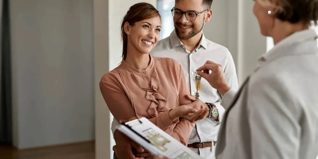 Pareja feliz recibe las llaves de su nuevo hogar, con un agente inmobiliario mostrando las escrituras de una casa.