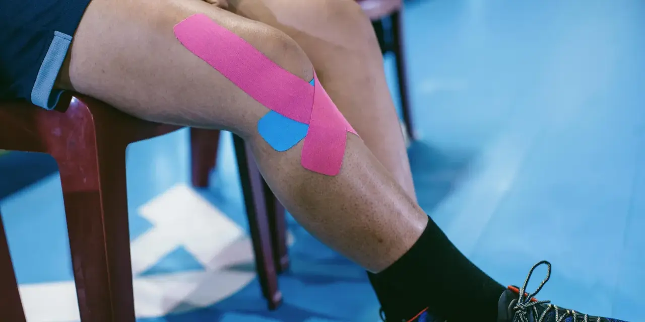 Sportowiec z plastrami na kolanie, przygotowujący się do ćwiczeń na chondromalację rzepki.