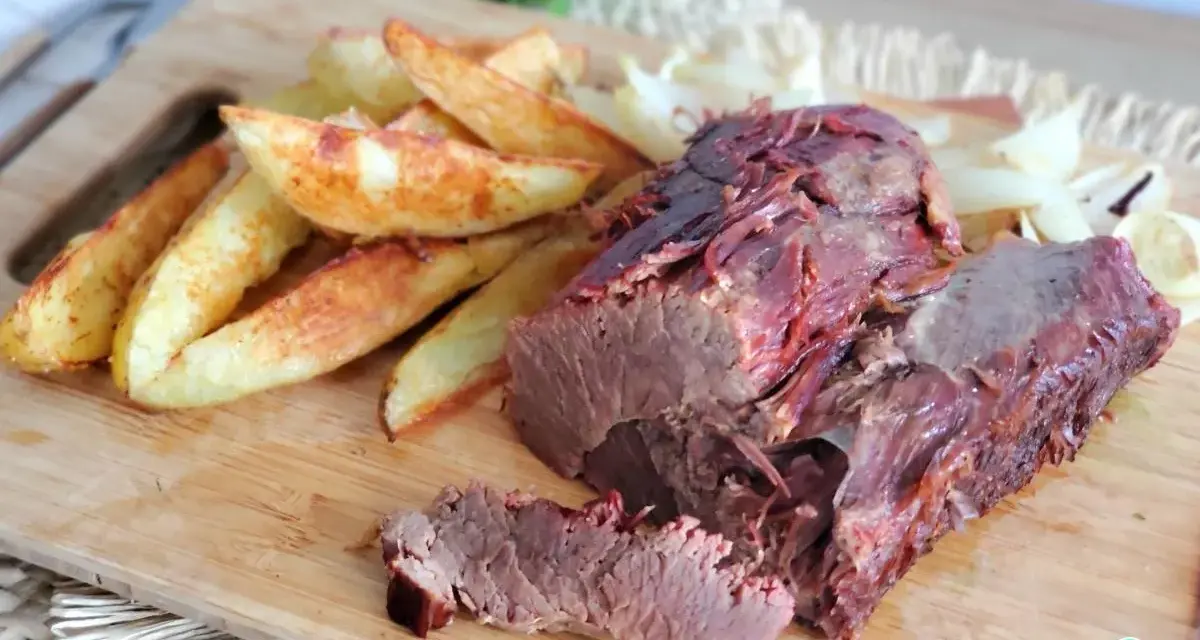 Rosbif jugoso y tierno servido con papas gajo y cebolla en una tabla de madera.