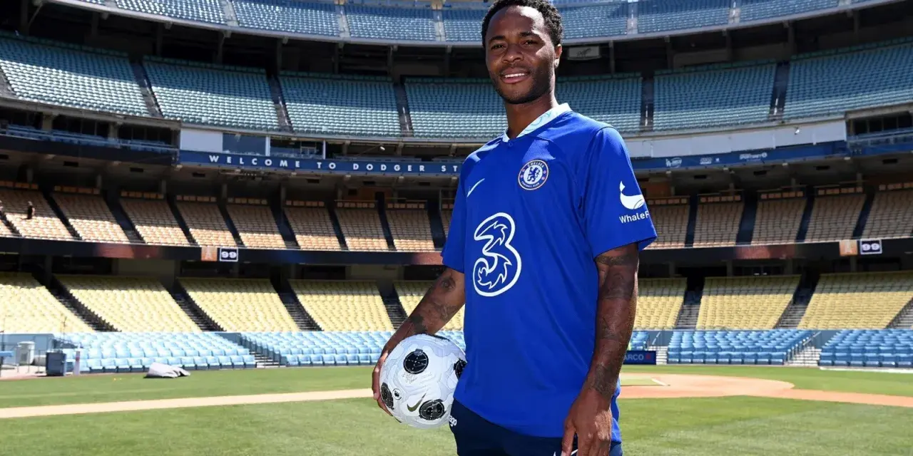 Raheem Sterling w niebieskiej koszulce Chelsea z piłką, na tle stadionu. Jego statystyki w klubie są obiecujące.