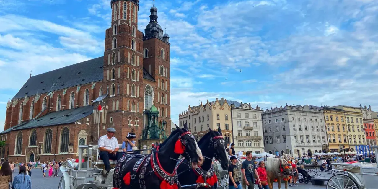 Horse-drawn carriages await tourists in Krakow's Old Town, a picturesque scene from a Poland trip, with St. Mary's Basilica towering in the background.
