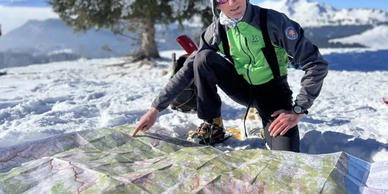 Un homme en tenue de ski pointe une carte sur la neige, planifiant son ascension vers le plus haut sommet de France.