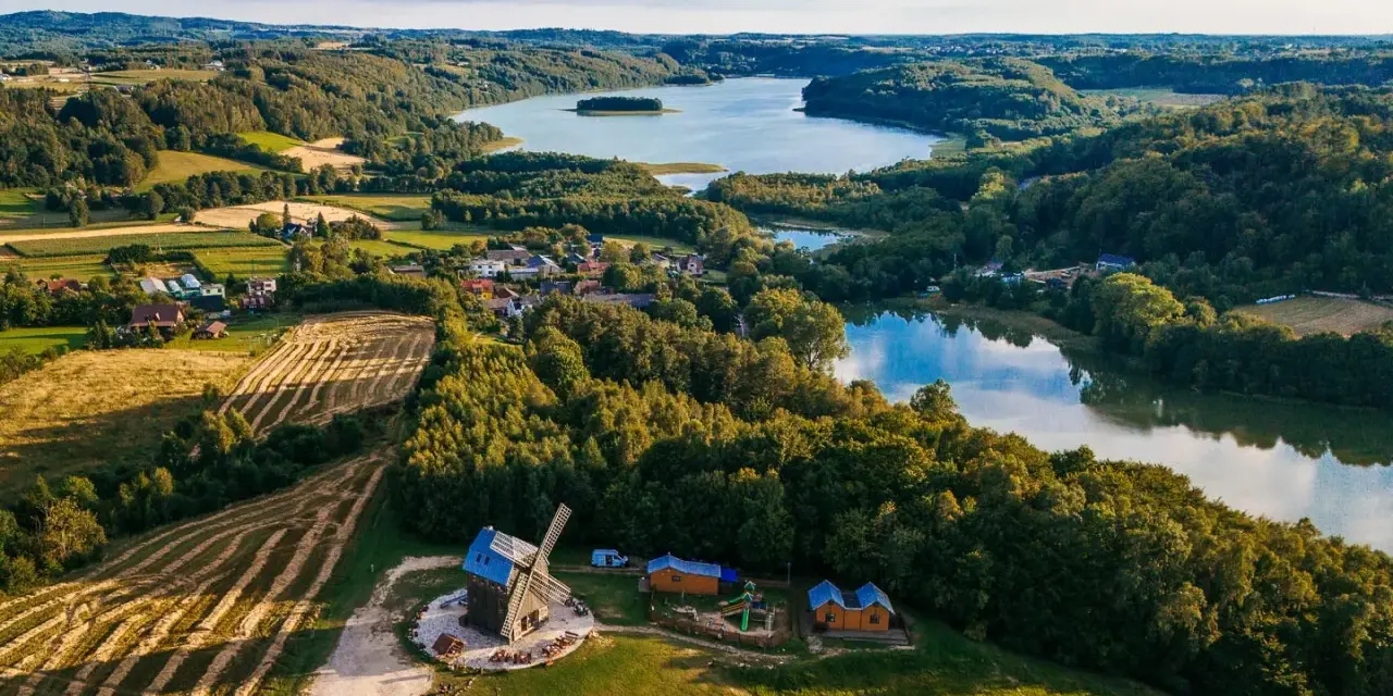 Malowniczy krajobraz kaszub z jeziorem, lasami, polami i drewnianym wiatrakiem.