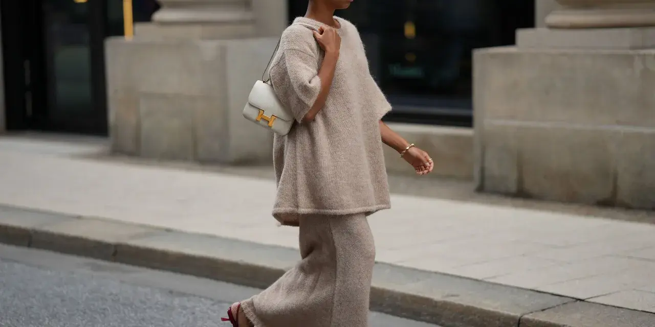 Donna con completo beige e borsa bianca, indossa scarpe rosse con tacco kitten, un dettaglio che aggiunge eleganza.