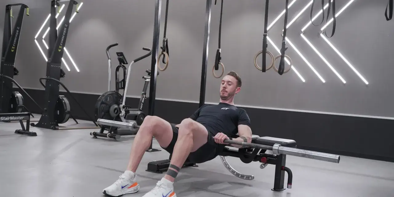 Man utför hip thrust med skivstång på en bänk i ett modernt gym.