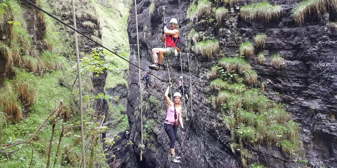 Abenteuer im **Postalmklamm Klettersteig**: Menschen seilen sich durch eine enge Schlucht ab, gesichert an Seilen, umgeben von steilen, bewachsenen Felswänden.