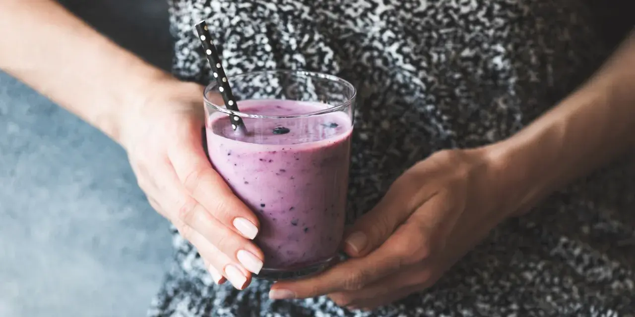 Ręce trzymają szklankę z fioletowym smoothie, które może być skuteczną miksturą na zaparcia.