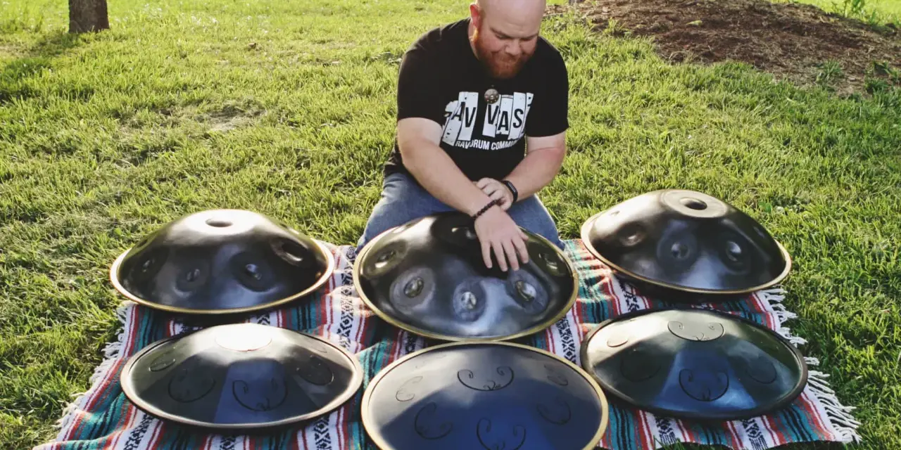 Mann spielt auf mehreren runden Metallinstrumenten im Freien.
