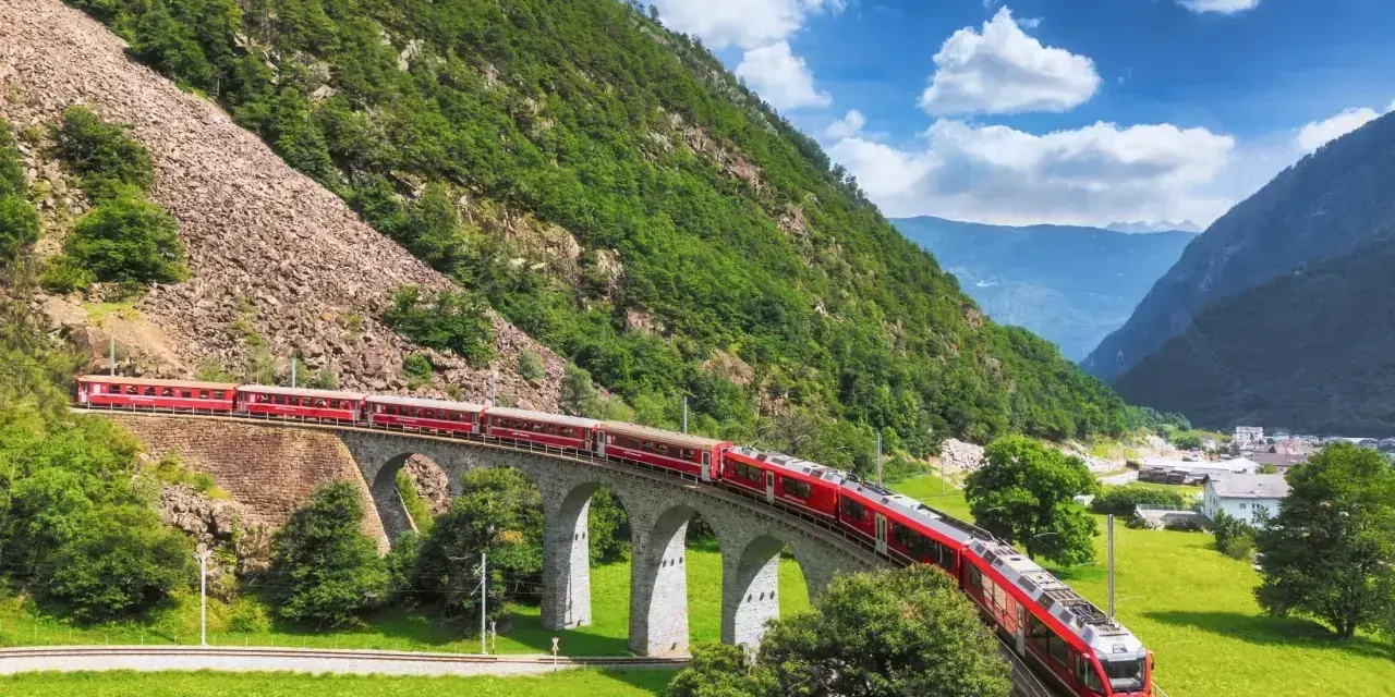 Czerwony pociąg Bernina Express przejeżdża przez kamienny wiadukt w Alpach. Sprawdź bernina express cena, by zaplanować podróż.