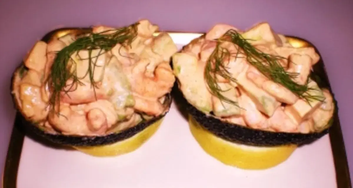 Zwei Avocadohälften gefüllt mit einem cremigen Krabbencocktail mit Avocado und Dill garniert, serviert auf Zitronenscheiben auf einem Teller.