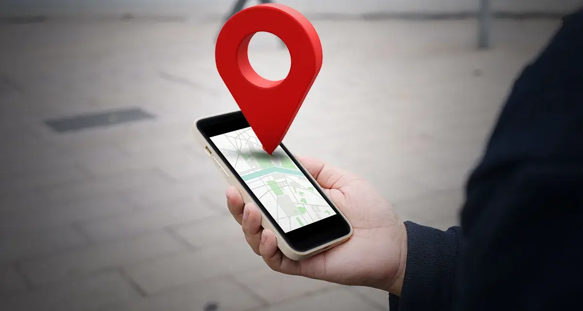Dłoń trzyma smartfon z mapą, a nad nim unosi się czerwona pinezka. To wizualizacja, jak wysłać pinezkę z lokalizacją.