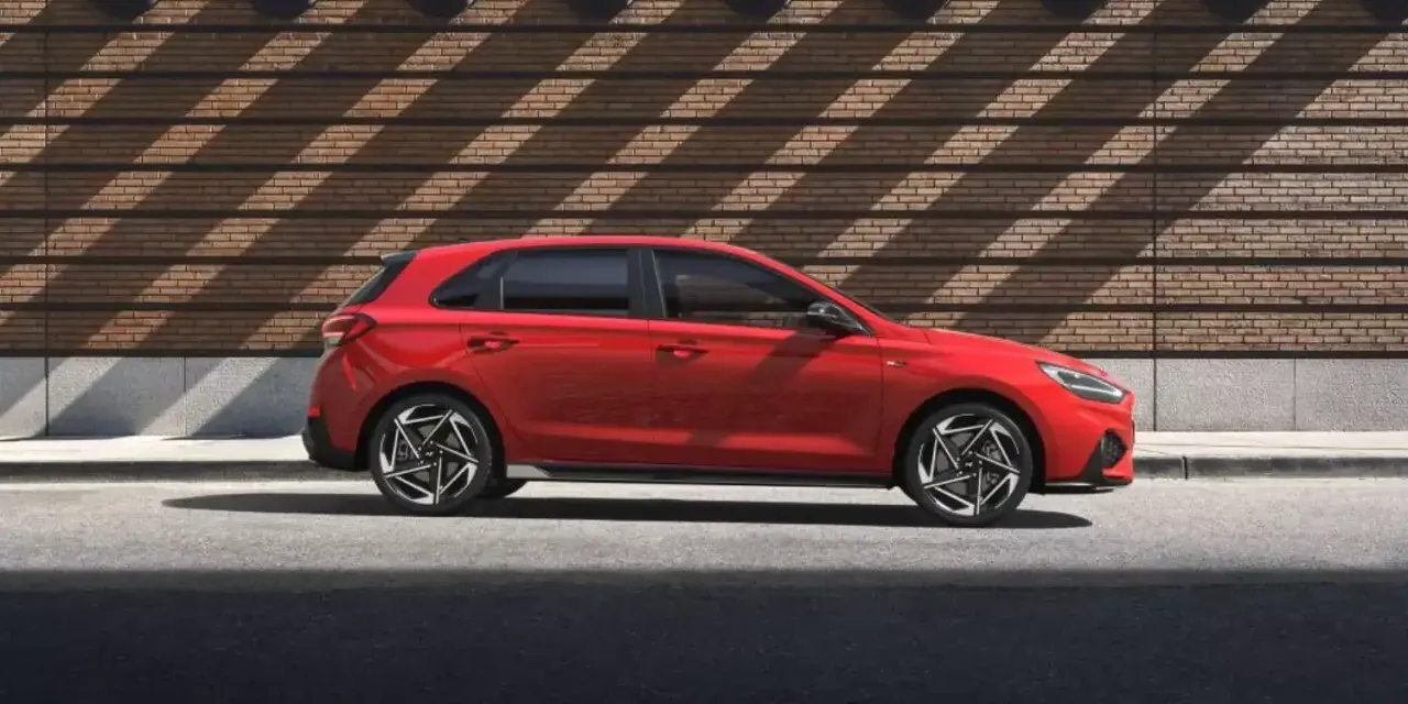 Czerwony Hyundai i30 stoi na tle ceglanej ściany z ciekawymi cieniami.