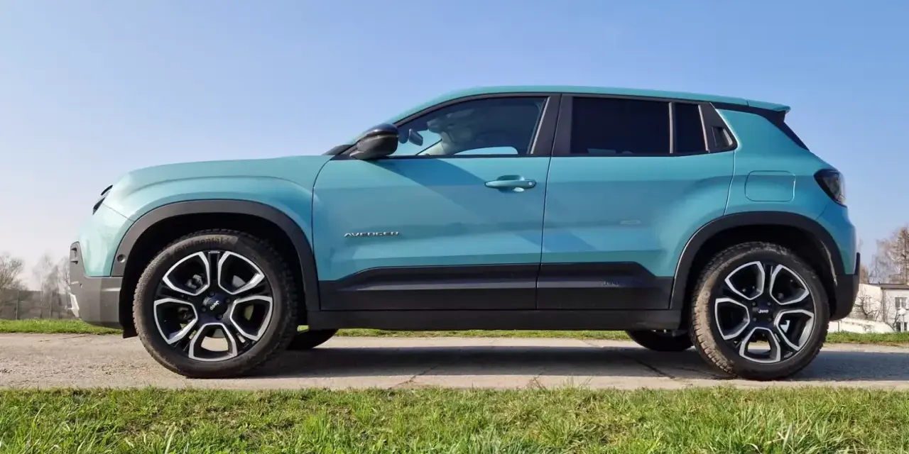 Turkusowy Jeep Avenger 4x4 z czarnymi felgami na tle nieba i trawy.