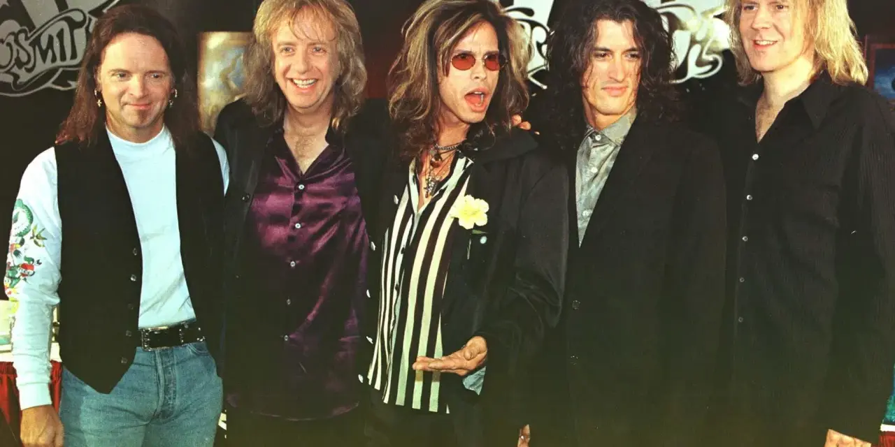 Steven Tyler mlody z zespołem Aerosmith, w charakterystycznych okularach i stroju, gotowy na scenę.