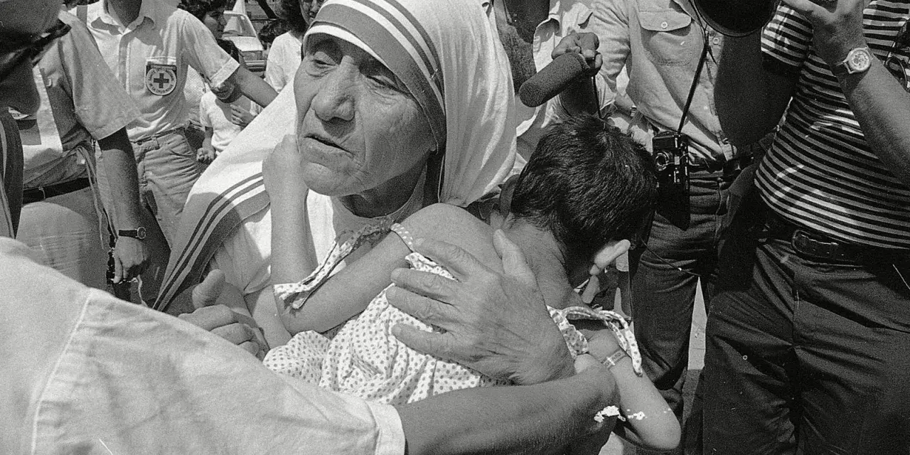 Missionaries of Charity founder, Mother Teresa, cradles a child amidst a crowd and media attention.