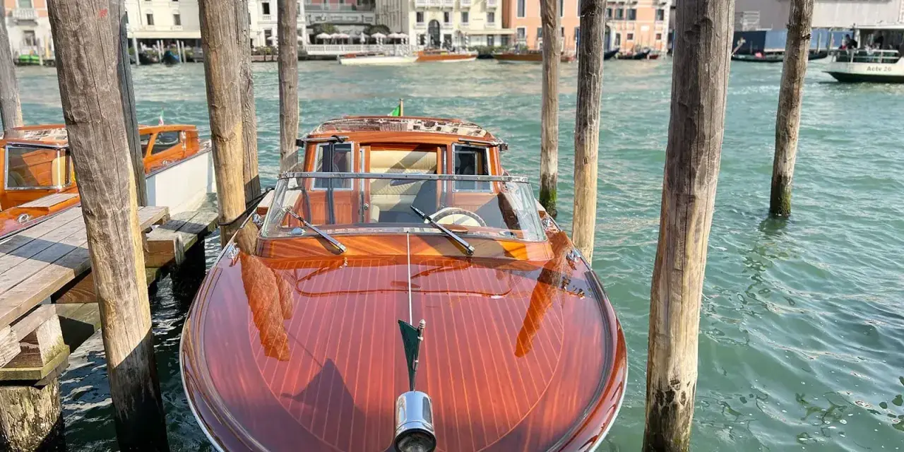 Un elegante taxi boat in legno lucido attende sul Canal Grande a Venezia, pronto a trasportare passeggeri tra i palazzi storici.