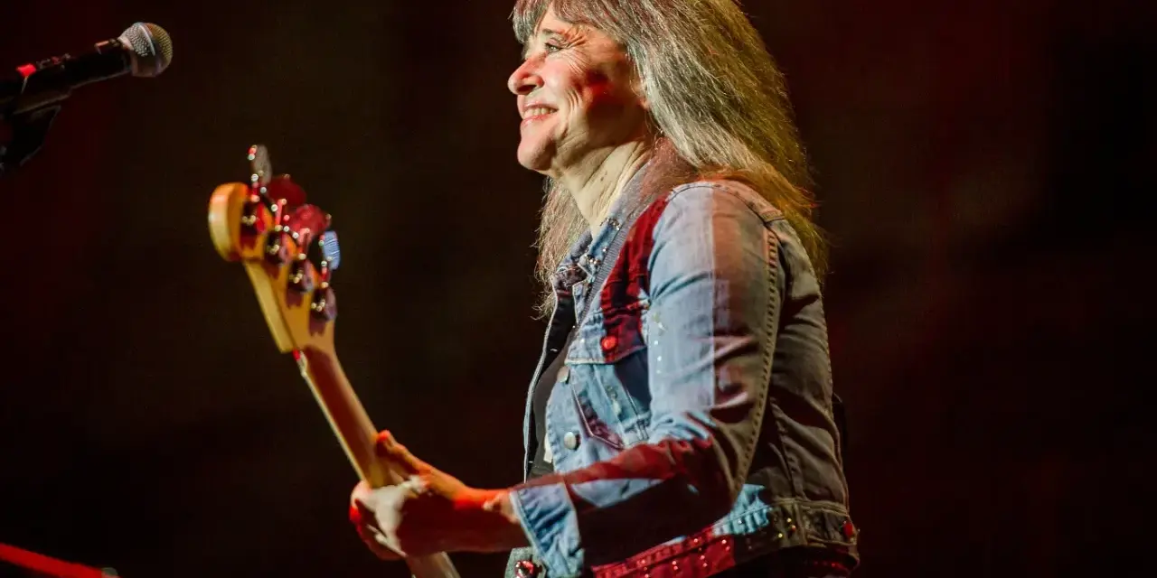 Suzi Quatro dzisiaj na scenie, z basem w ręku, uśmiecha się do publiczności. Rock'n'rollowa legenda w dżinsowej kurtce.