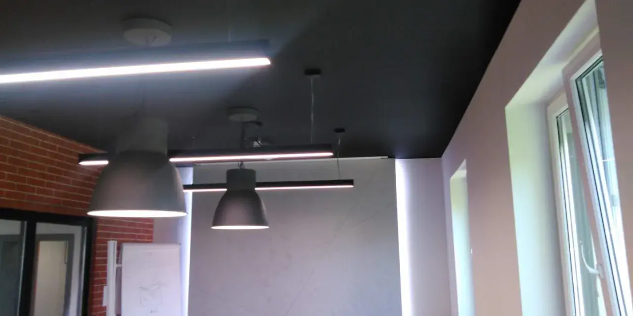 Nowoczesne biuro z czarnym sufitem (RAL 9004), wiszącymi lampami i ceglaną ścianą.