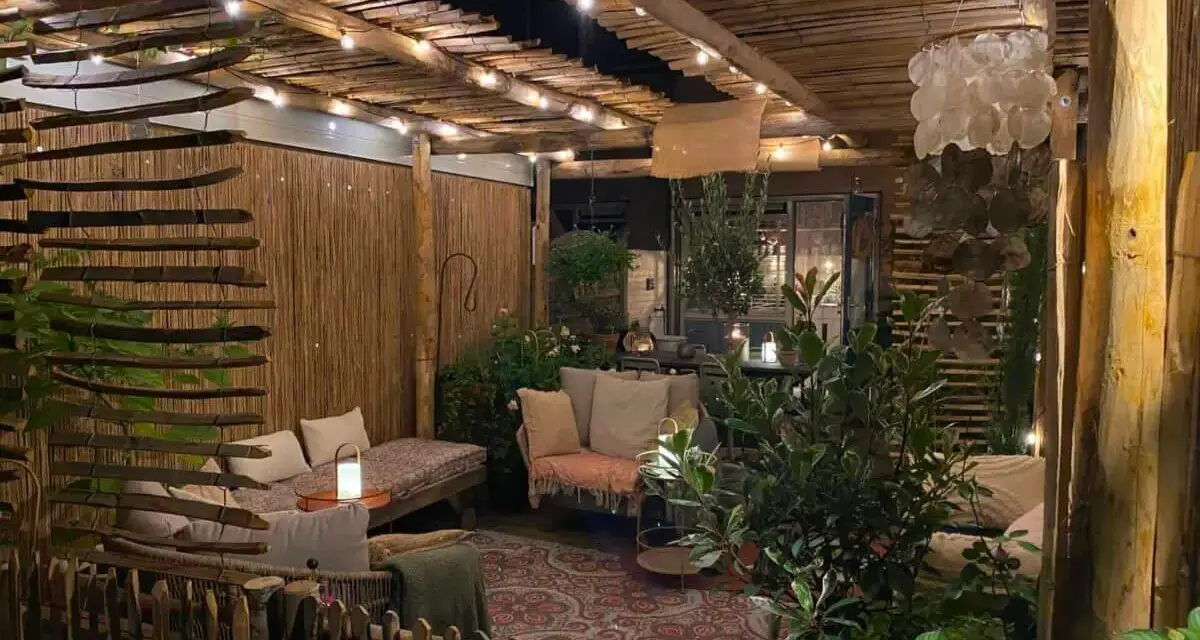Une terrasse de jardin aménagée en coin cocooning, avec des banquettes confortables, des lumières douces et une ambiance chaleureuse.
