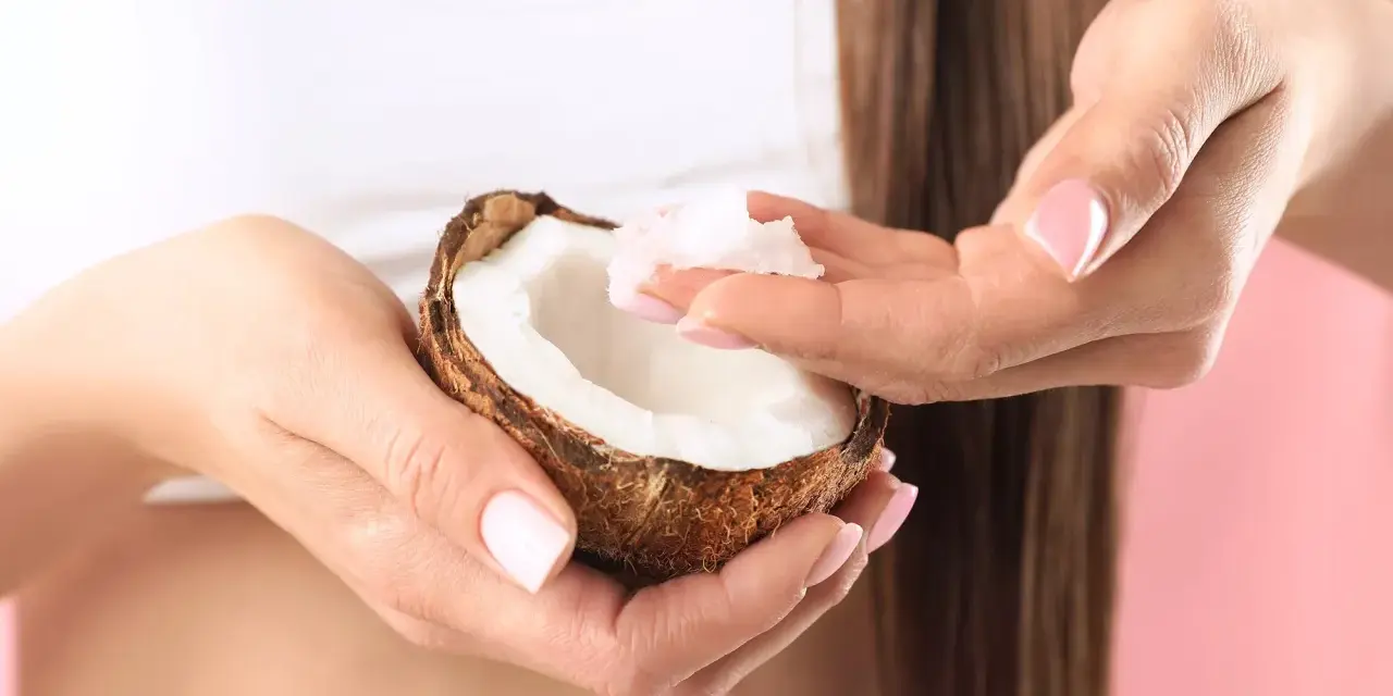 Mani con unghie curate prendono polpa di cocco da una noce, ingrediente perfetto per una maschera capelli fai da te nutriente.